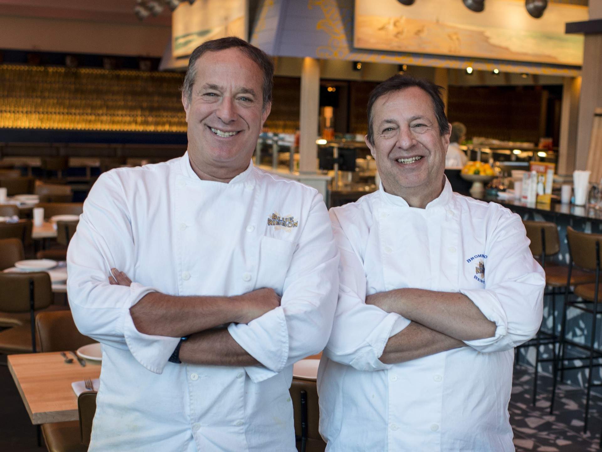 Chefs and restaurateurs Bruce (left) and Eric Bromberg at their Boston restaurant Pescador. Both are wearing white chefs coats and smiling at the camera.