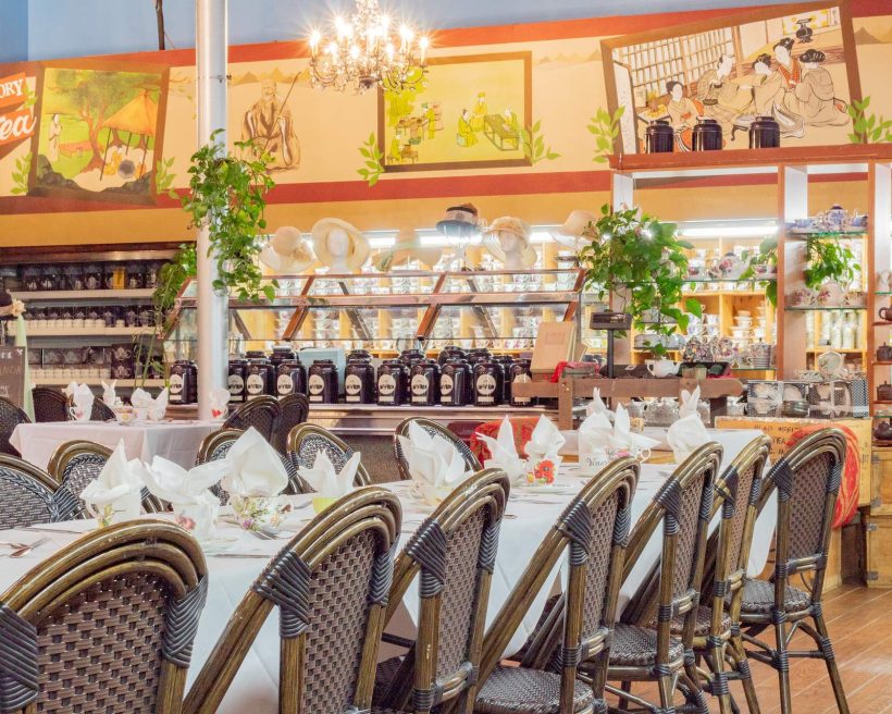An interior photo of a Chado Tea Room location in Torrance featuring wicker chairs and tea sets seen on shelves in the background