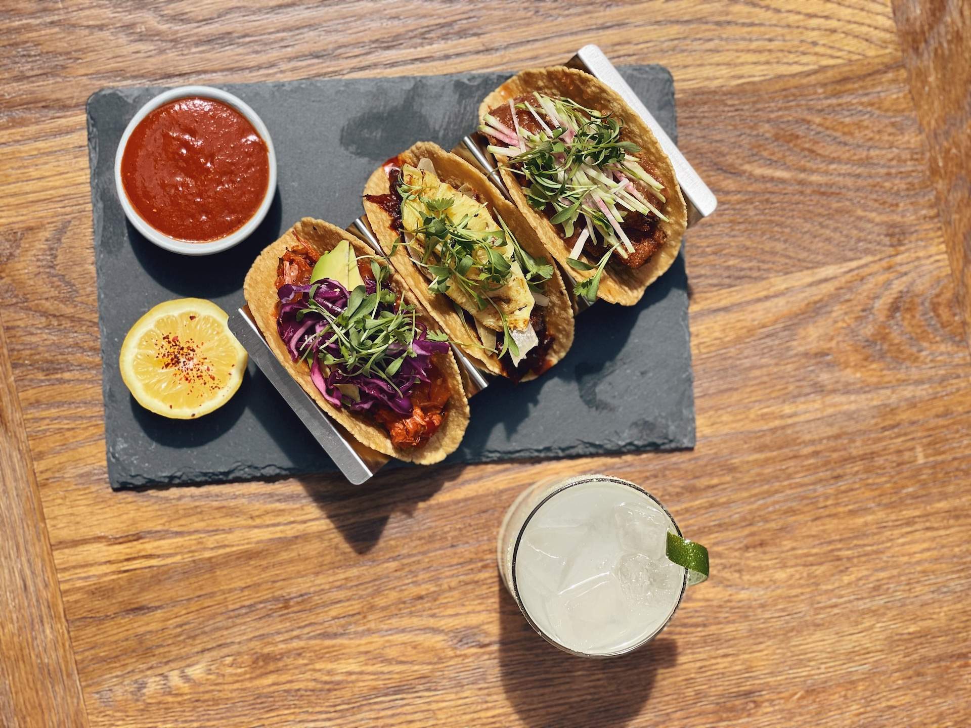 Three tacos placed side by side on a slate plate set on a wooden table at Los Angeles restaurant Gracias Madre