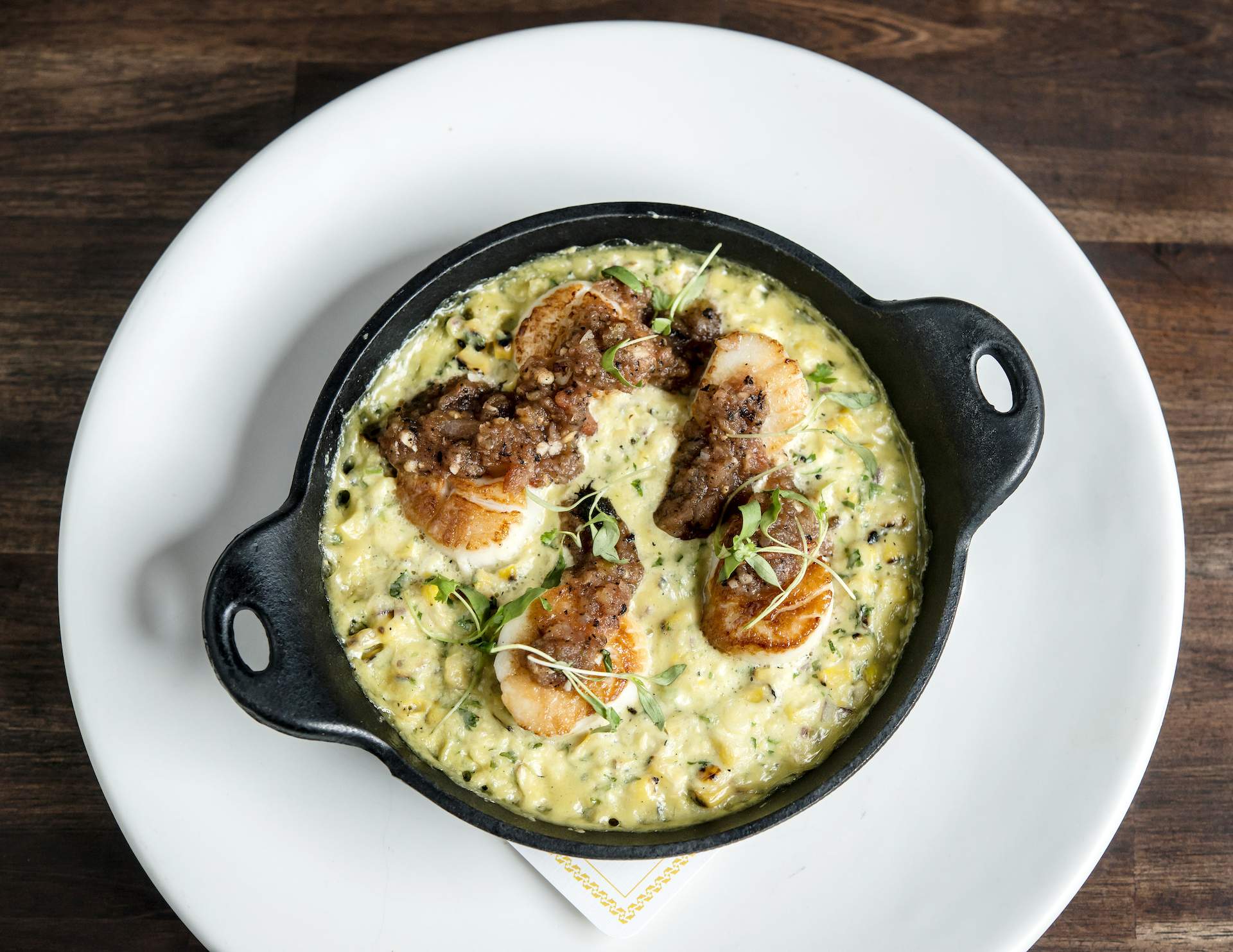 A black cast-iron dish featuring a yellow sauce and pieces of blackened scallops. The dish is at the Boston restaurant Pescador.