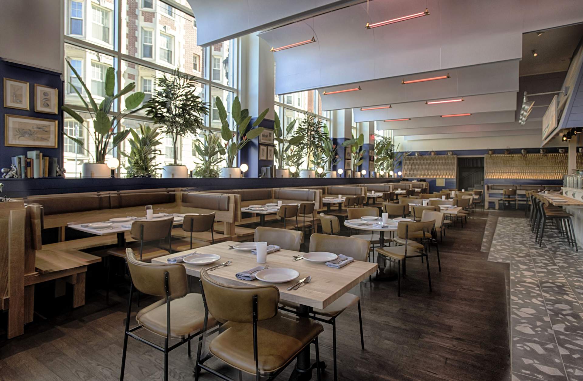 The interior of the Boston restaurant Pescador seen here with light brown tables and chairs, expansive windows in the background and plants along the windowsill