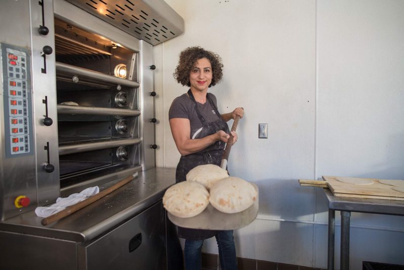 The chef Reem Assil taking out bread from an oven at her restaurant in San Francisco's Mission District