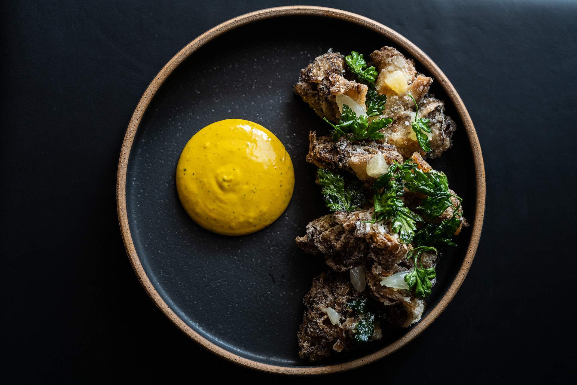 A plate of roasted mushrooms at the Los Angeles restaurant Asterid. There is a yellow sauce next to it.