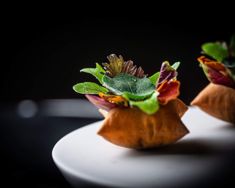 A composed dish at San Diego's Addison featuring mixed green leaves atop of a crispy shell