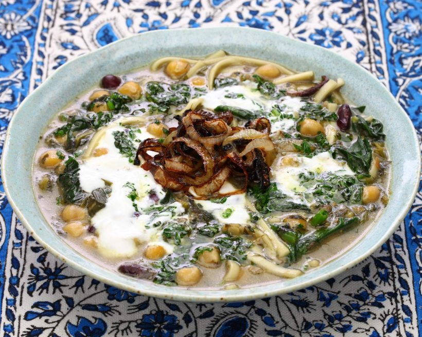 A photo of an Iranian soup that's green in color with some white cream. The soup is call Ash Reshteh