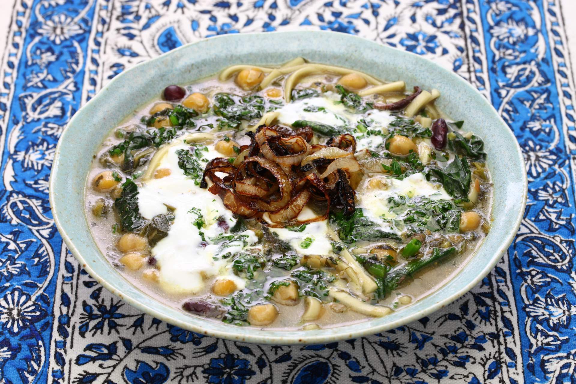 A photo of an Iranian soup that's green in color with some white cream. The soup is call Ash Reshteh