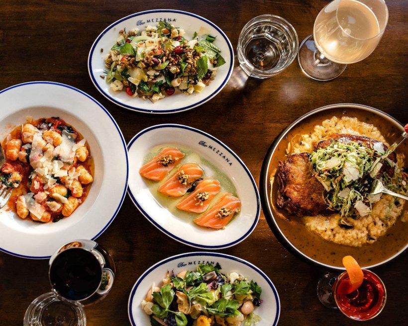 Numerous plates of food placed on a wooden table at Bar Mezzana in Boston