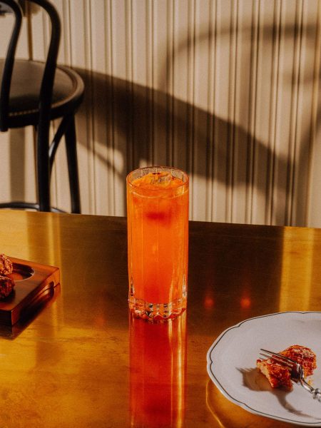 A orange drink in a tall glass sits on a golden table