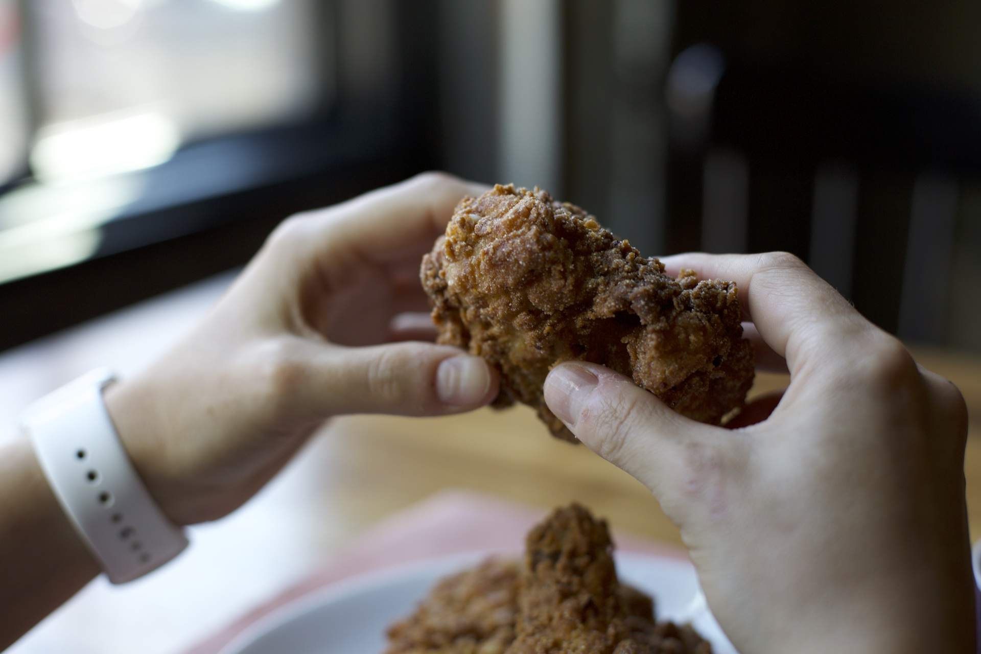 Two hands shown holding a piece of crispy fried chicken at Chicago restaurant Split Rail