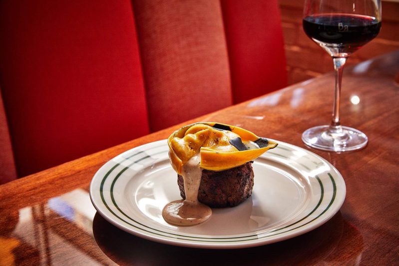 A ravioli sits on top of a filet mignon as sauce from the ravioli spills onto the filet