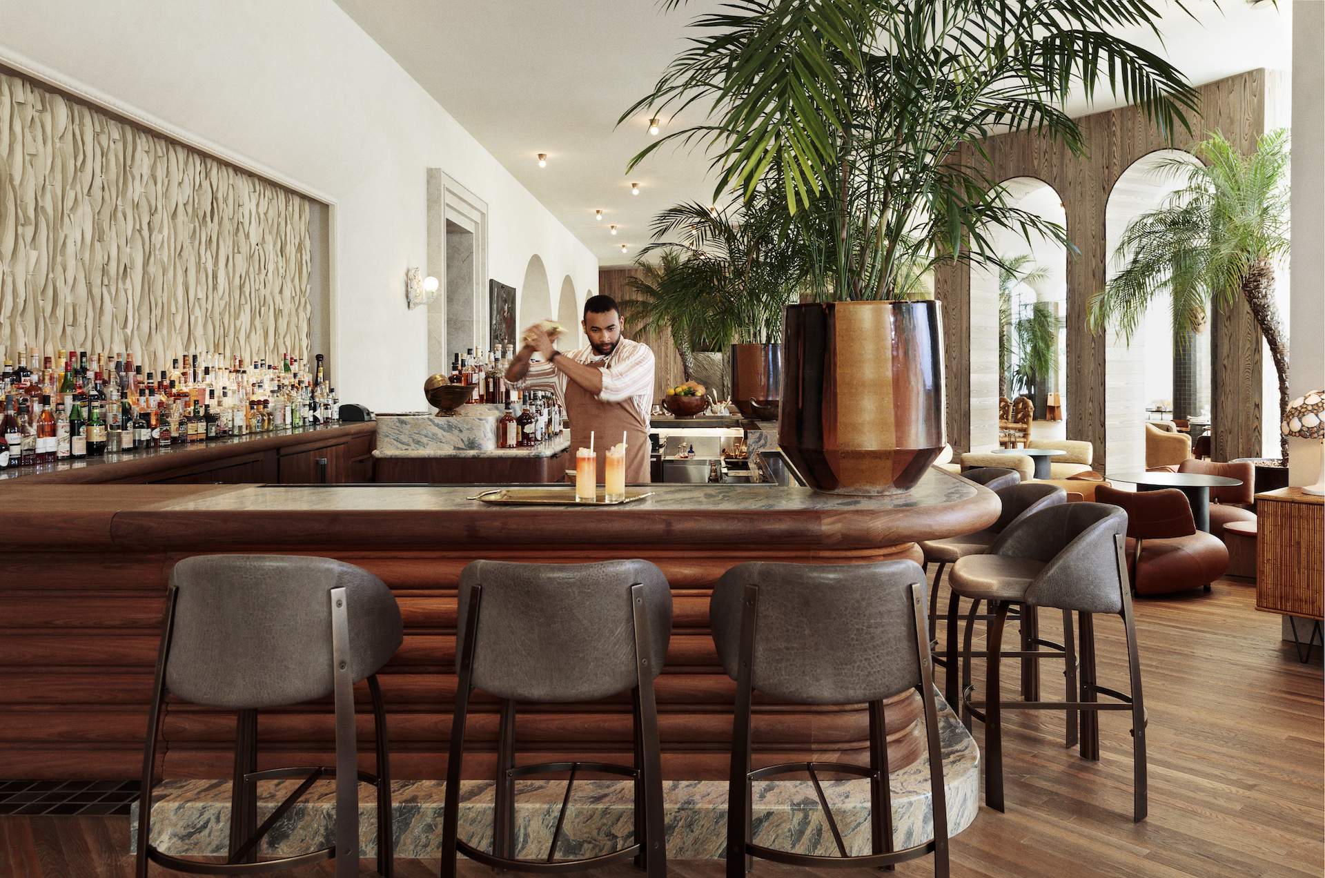 The interior of the restaurant Palma in Los Angeles with a wooden bar counter and a giant palm tree in the background.