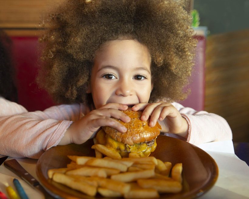 A child eats a cheeseburger with fries