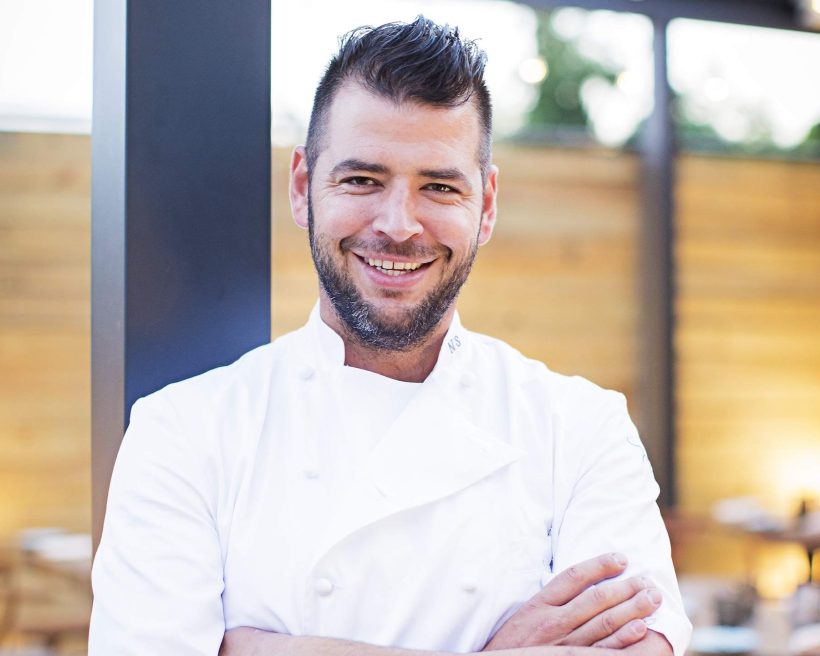 The Washington DC chef Nicholas Stefanelli in a white apron smiling at the camera.
