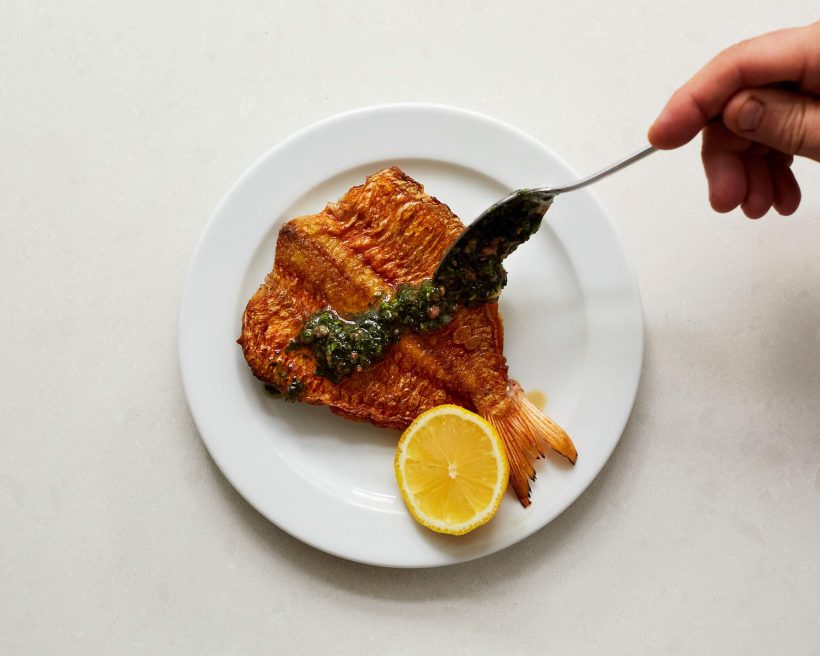 A hand spoons green sauce over fish