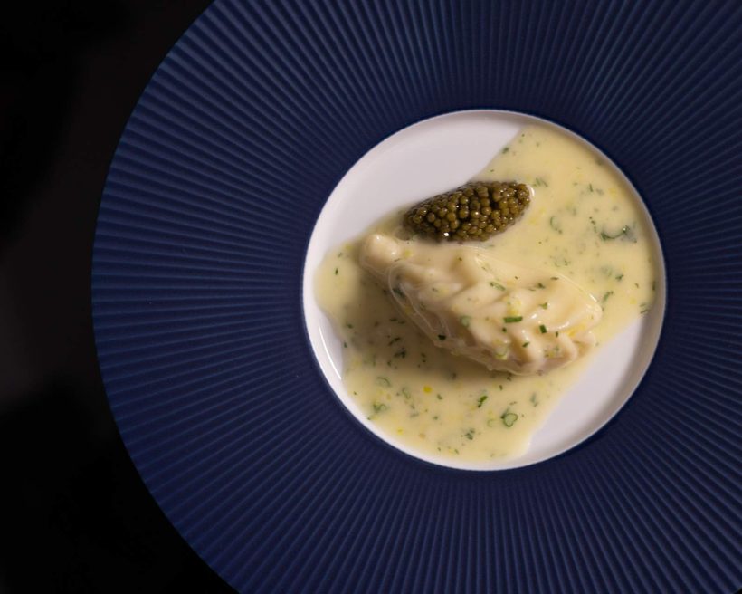 Mashed potatoes shaped in an oval next to black caviar in a yellow sauce set on a white plate at NYC fine dining restaurant Al Coro