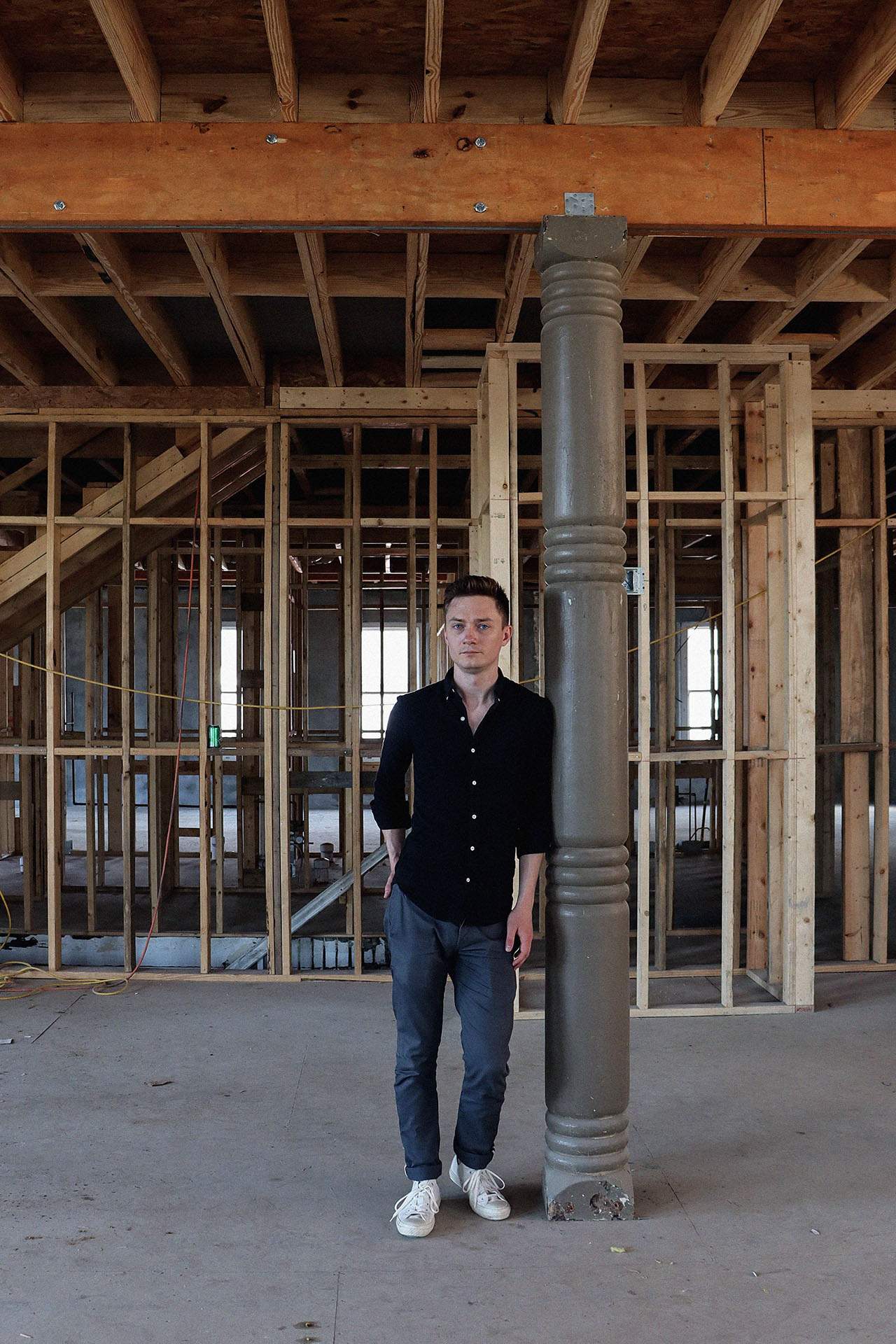 A man stands in a restaurant construction site, leaning against a pole