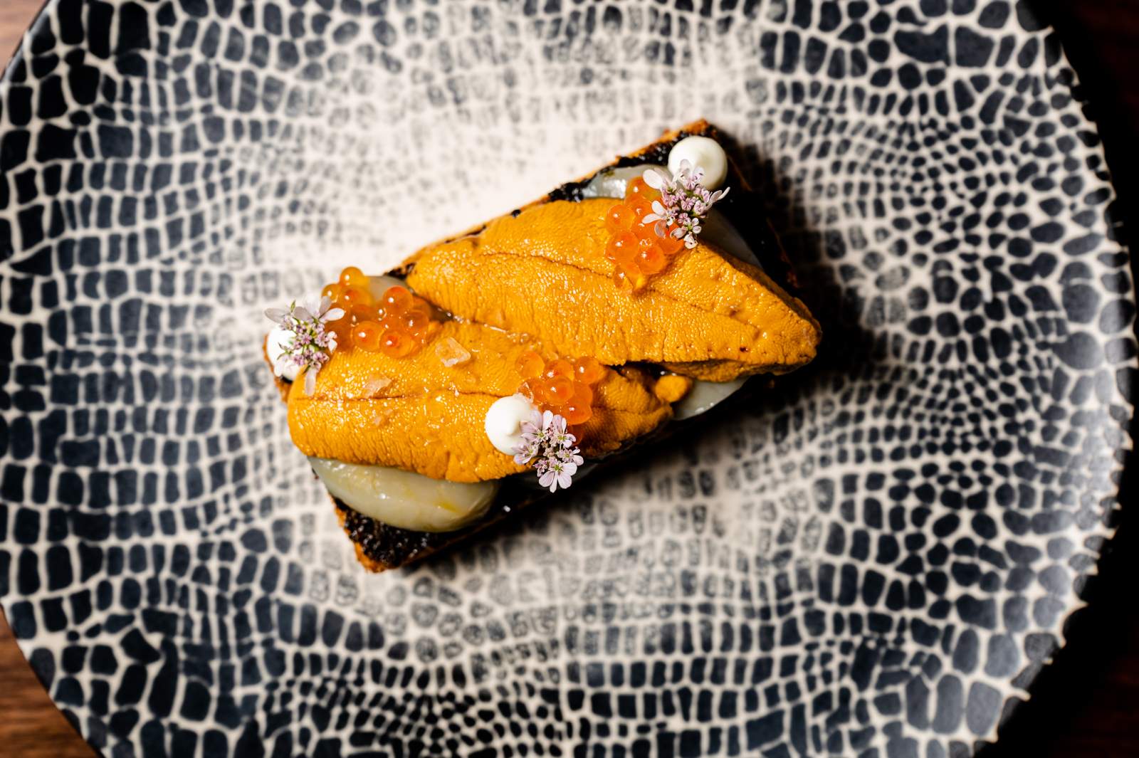 A black-and-white speckled dish with uni scallop toast topped with trout roe at Bansang in San Francisco