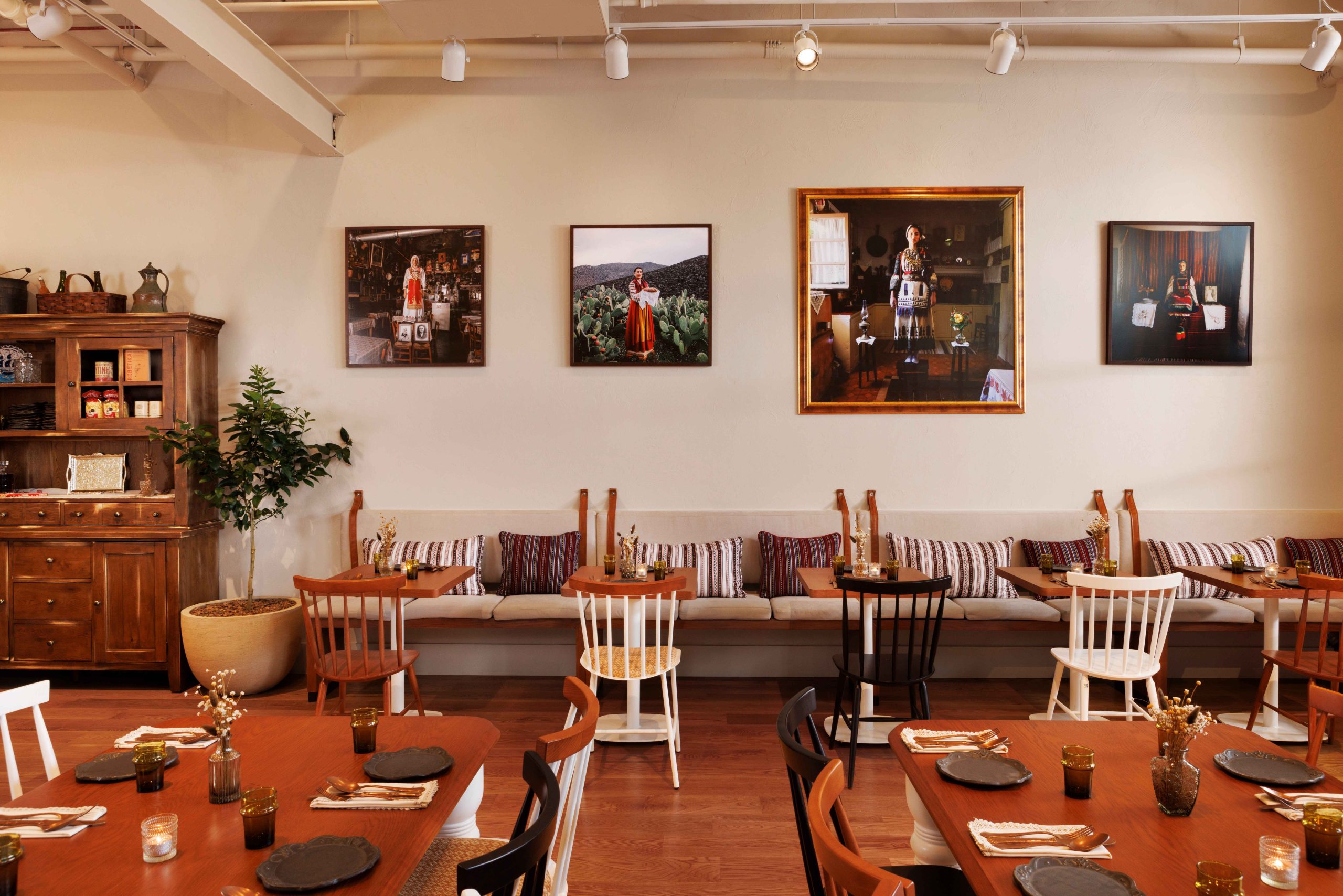 Striped pillows, wooden furniture, and portraits of Greek women at Bar Vlaha in Boston