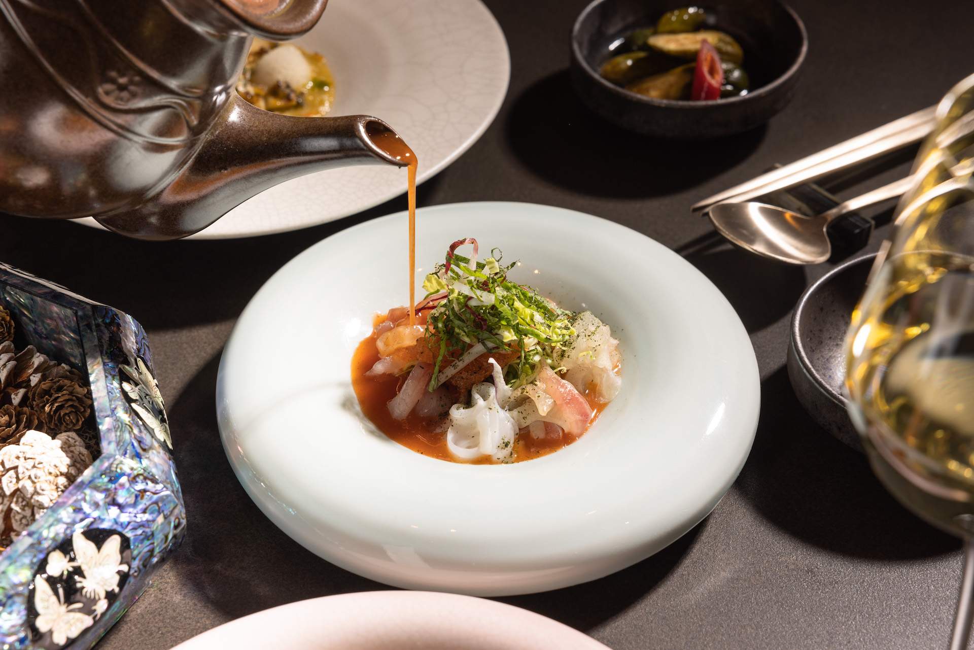A white bowl with food inside and a tea kettle pouring liquid over it at NYC Korean restaurant Anto