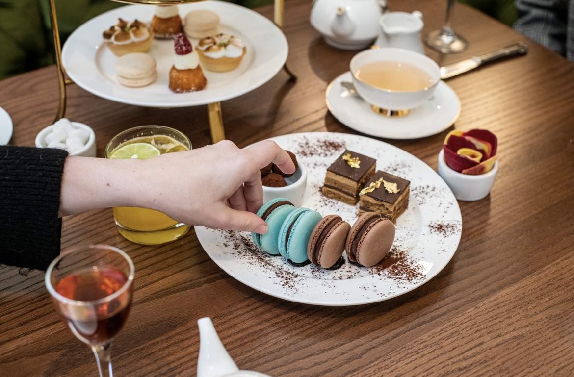 A hand reaches for a blue macaron on a table filled with pastries at Silver Dove in Boston.