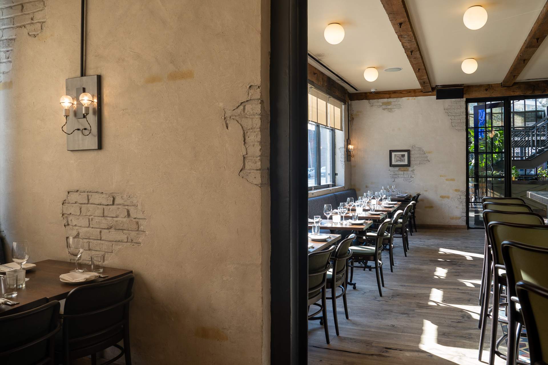 The interior of the Chicago restaurant the Dawson with light brown exposed brick walls and large windows that bring in a lot of light.