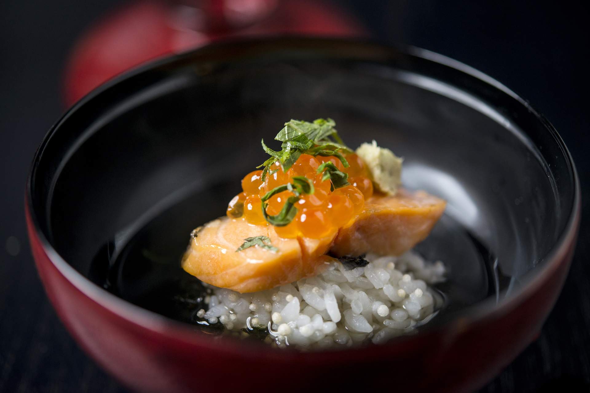 A piece of orange fish and orange fish eggs atop rice in a black bowl at NYC restaurant Ueki.