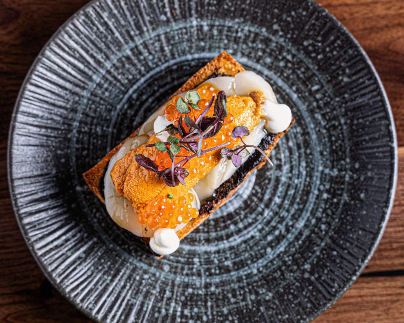 A black plate with an uni dish on top at San Francisco restaurant Bansang