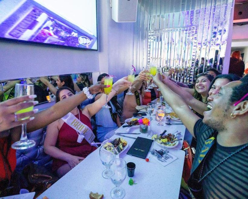 A group of people sitting at a long table at Chicago bar Kit Kat Lounge raising their glasses to cheers.
