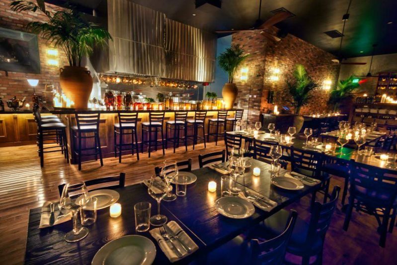 The interior of the LA Italian restaurant Dal Milanese featuring wooden floors, exposed brick walls, and black tables and chairs.
