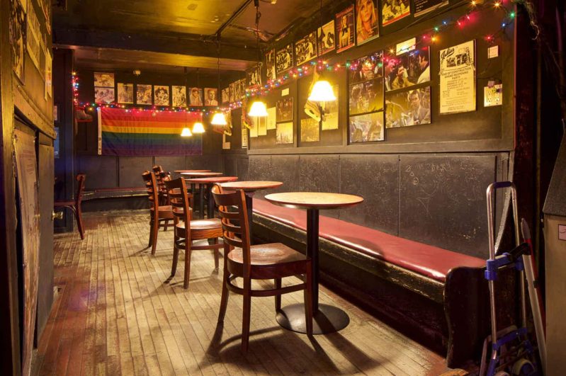 The wood-clad interior of historic NYC LGBTQ bar Julius’ featuring a rainbow flag and photos on the wall.