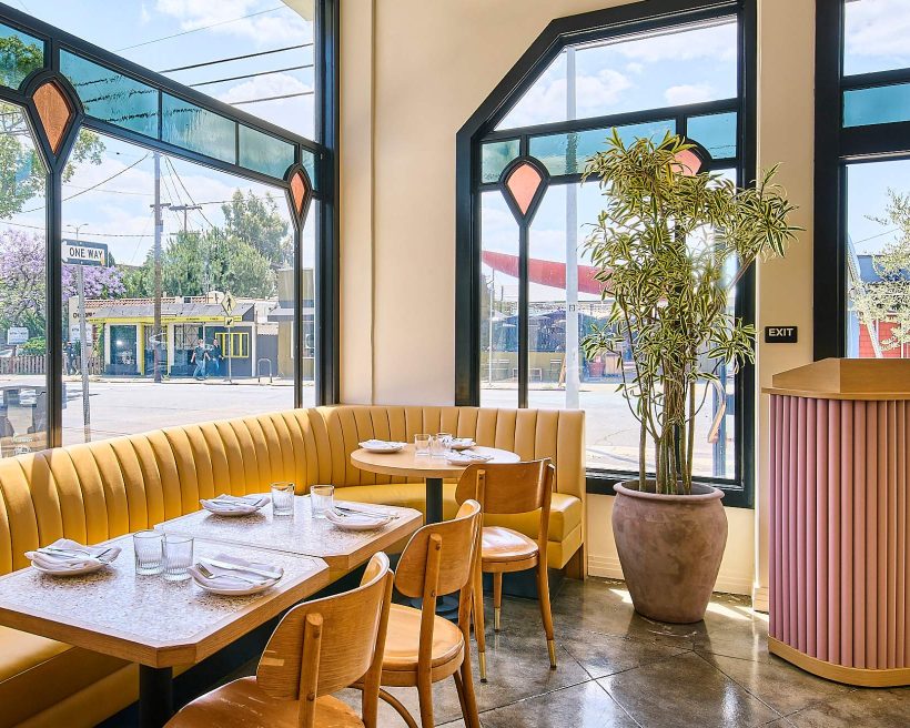 A yellow banquette next to a stained glass window at Saffy's in Los Angeles
