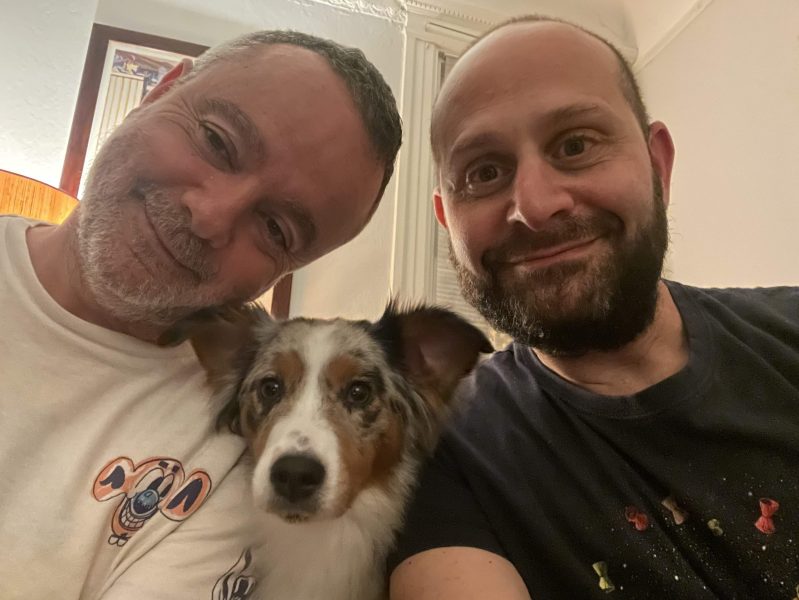 Co-owners of San Francisco restaurant Canela Paco Cifuentes and Mat Schuster sitting next to each other on a couch with their dog in between them.