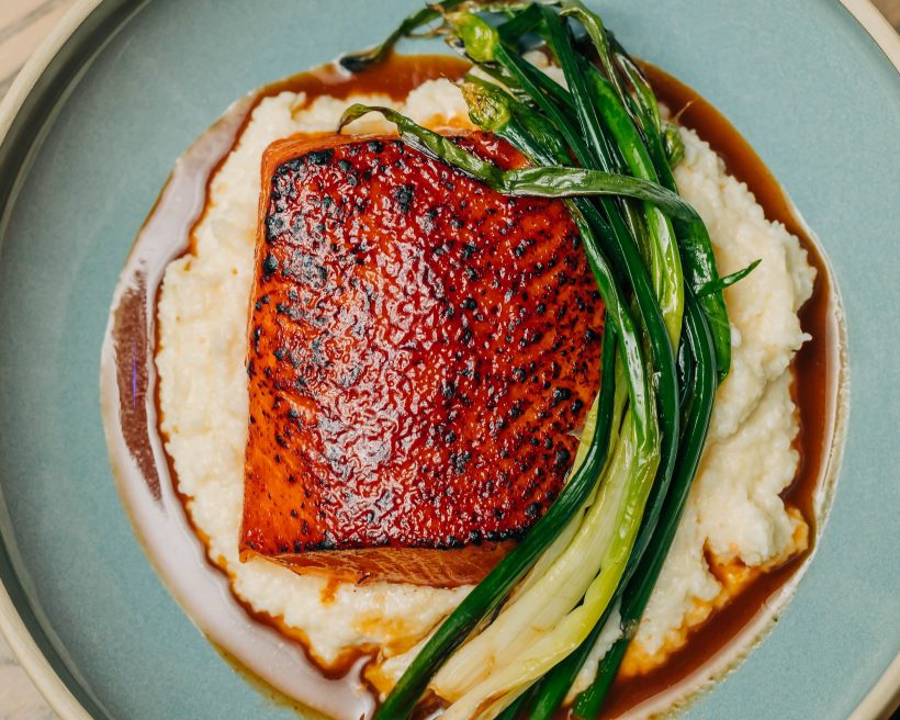 A piece of grilled salmon sitting on potato puree alongside scallions at Chicago restaurant The Oakville Grill & Cellar
