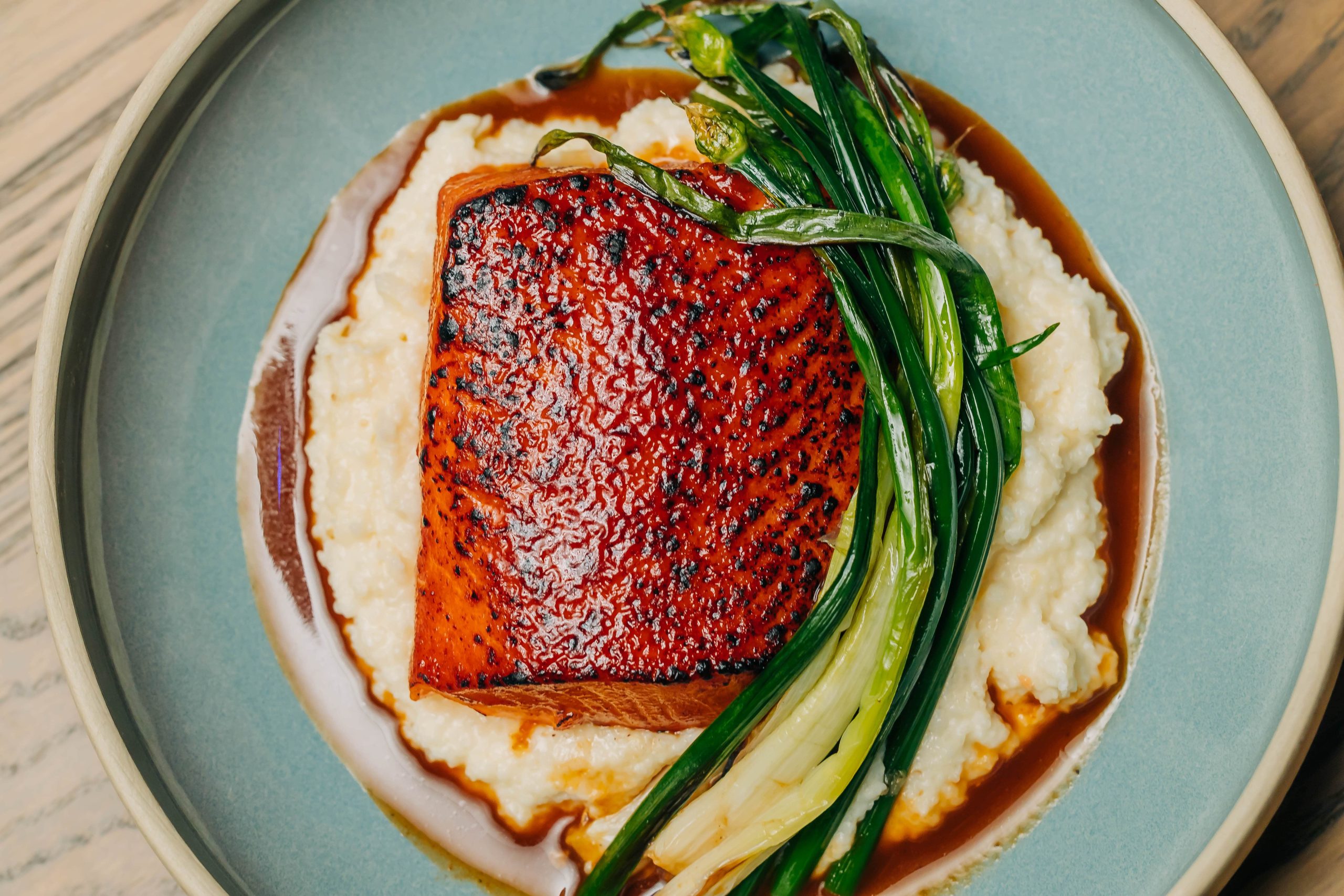 A piece of grilled salmon sitting on potato puree alongside scallions at Chicago restaurant The Oakville Grill & Cellar