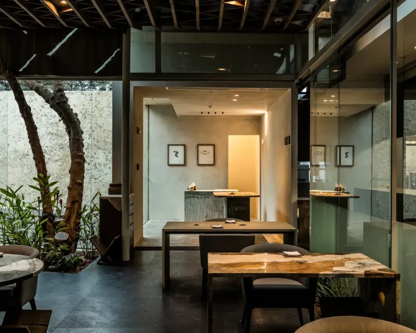 The interior of the Lima, Peru restaurant Central with light wood tables, a tall tree in a courtyard in the back, and dark floors.
