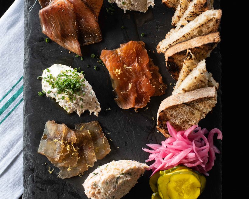 A board featuring various seafood patés, grilled bread, pickled onions, and crème Fraîche at Row 34 in Boston