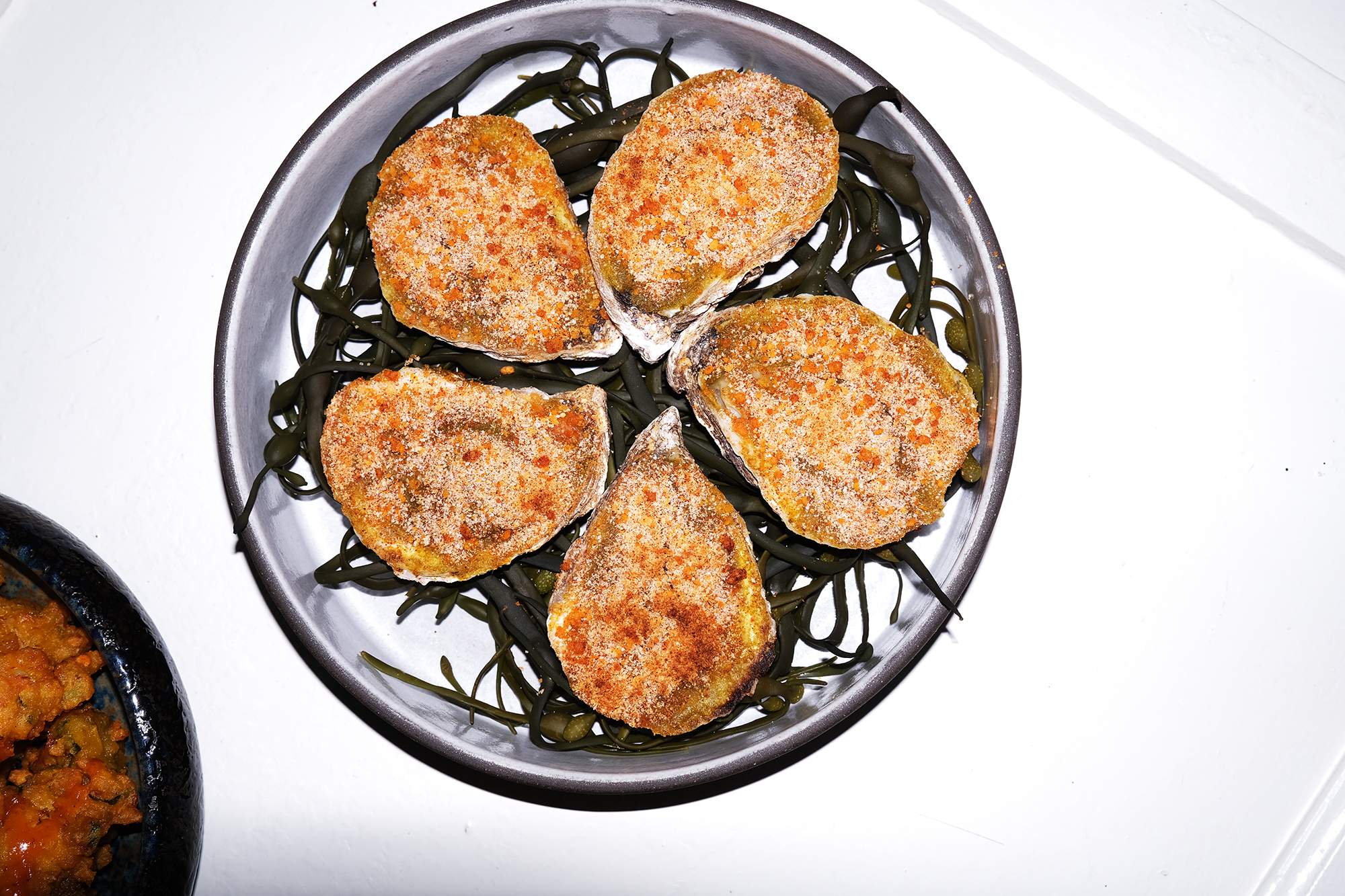 A white plate with five grilled oysters at the NYC restaurant Sona.