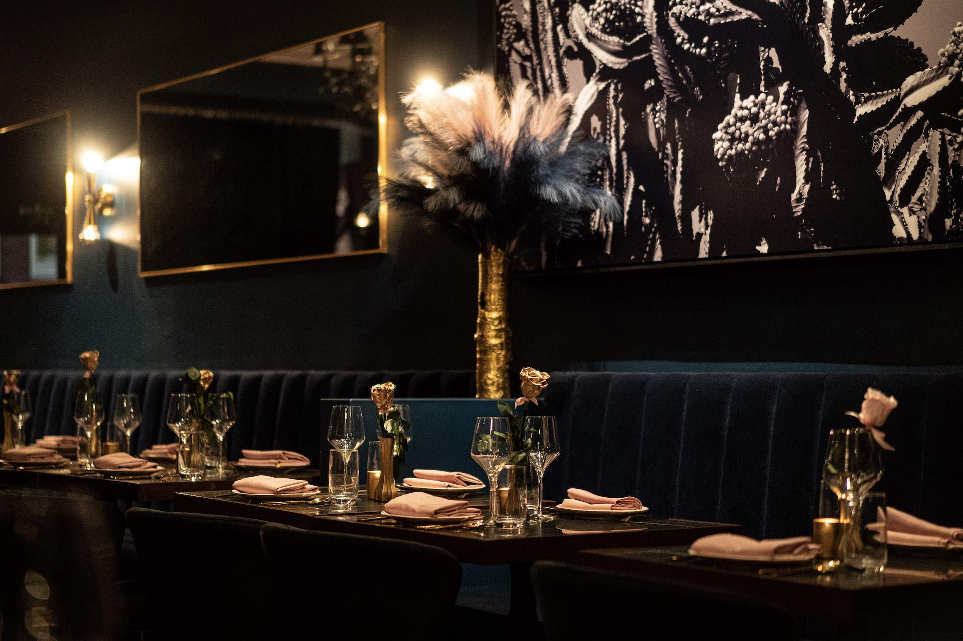 The interior of the NYC restaurant 9 Jones featuring green velvet banquettes, gold-framed mirrors, and pink roses on the table.
