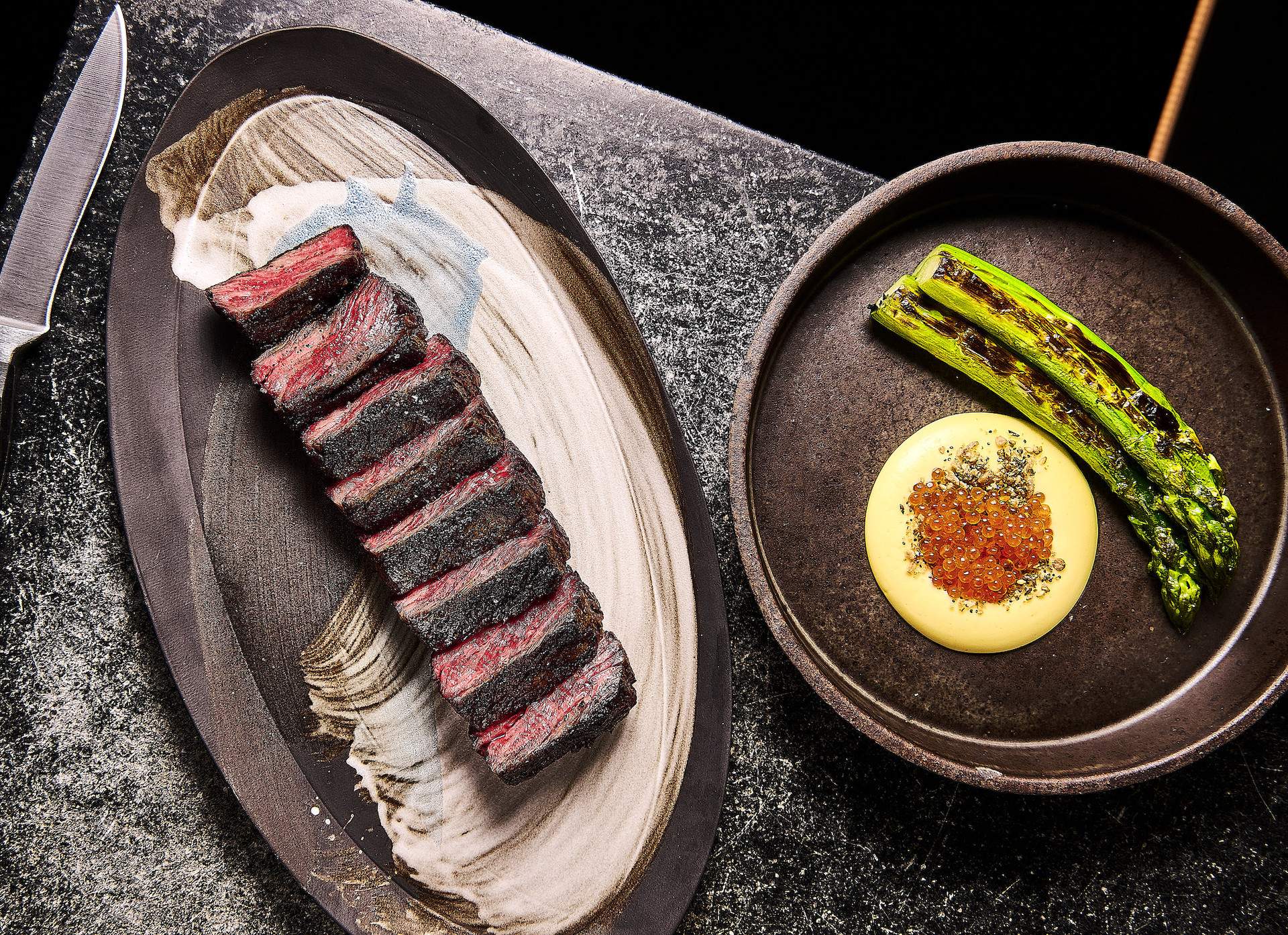 Plates of sliced steak and seared asparagus placed next to each other at San Francisco restaurant Niku Steakhouse.