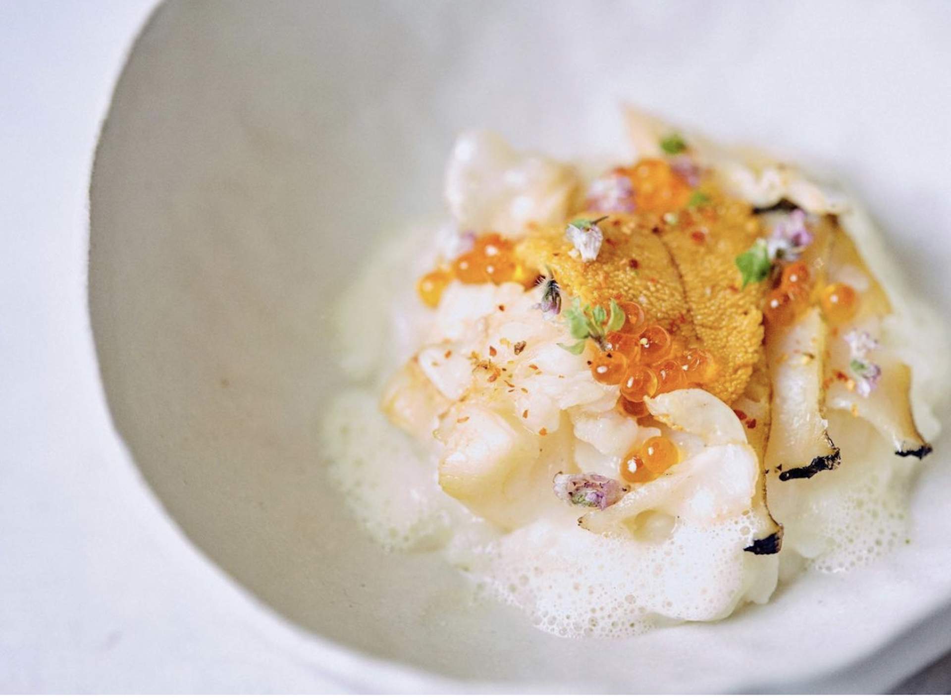 A seafood dish with orange caviar placed on a white plate at Los Angeles restaurant Orsa & Winston.