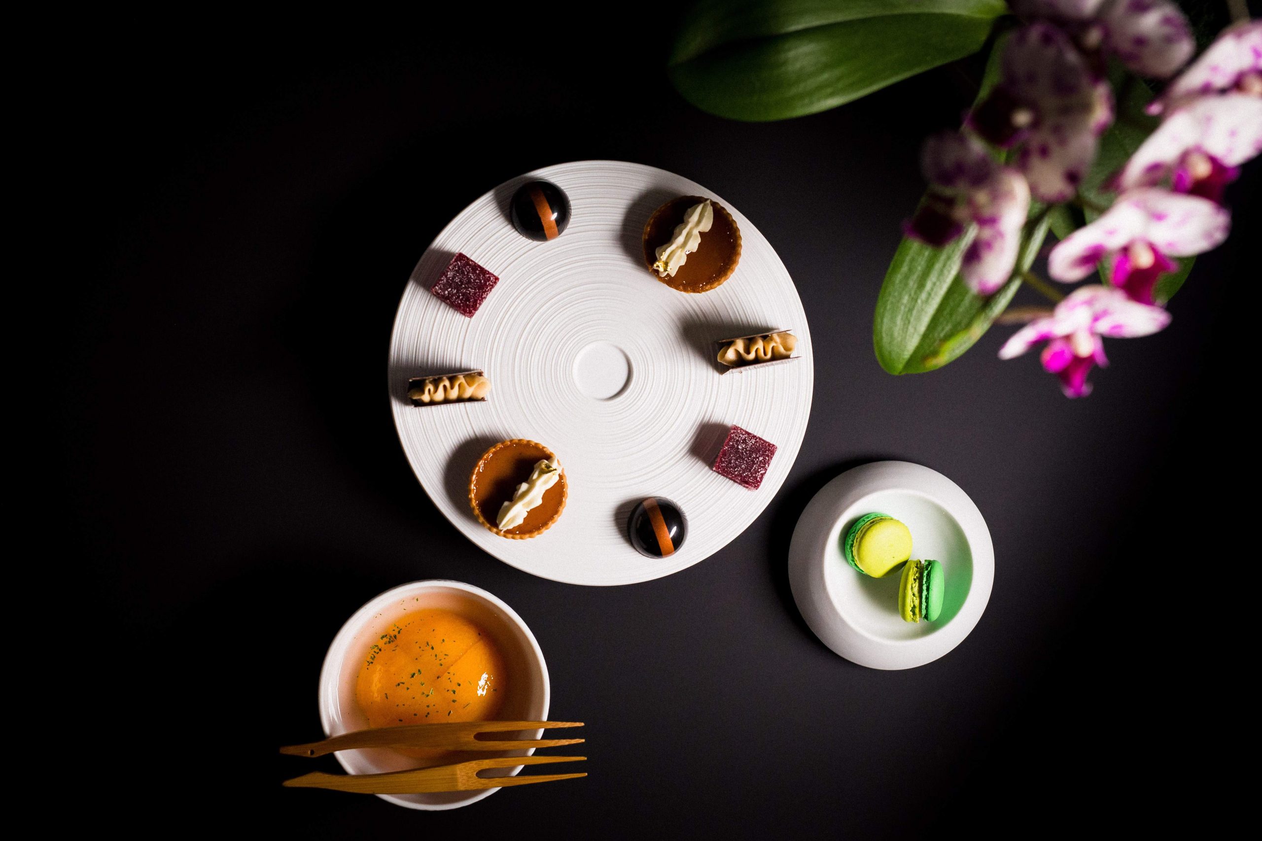 Three plated dishes on a black table alongside a vase of flowers at Los Angeles restaurant Providence.