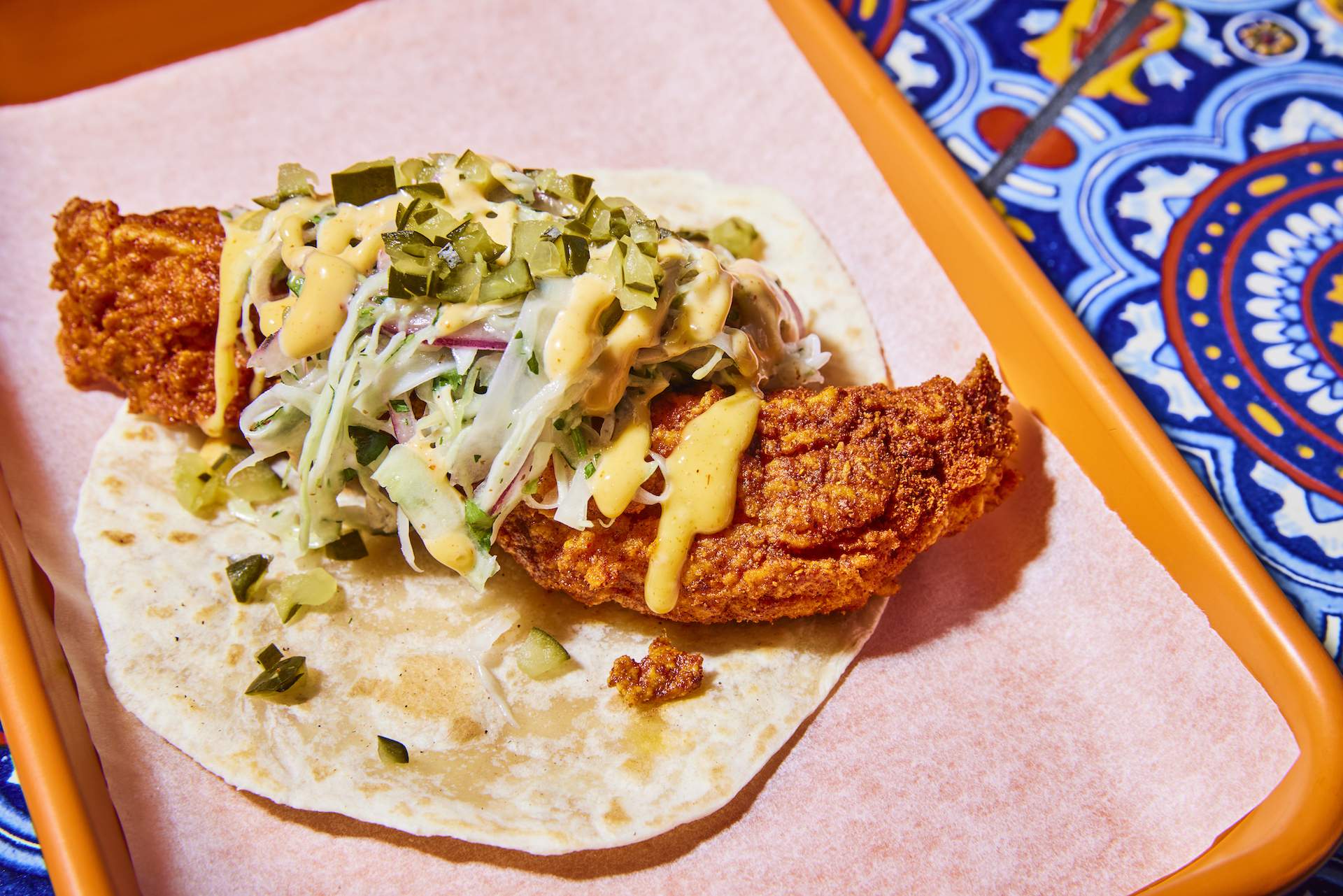 A piece of fried chicken placed in a tortilla with some slaw and pickles on top at Los Angeles restaurant The Brown Sheep