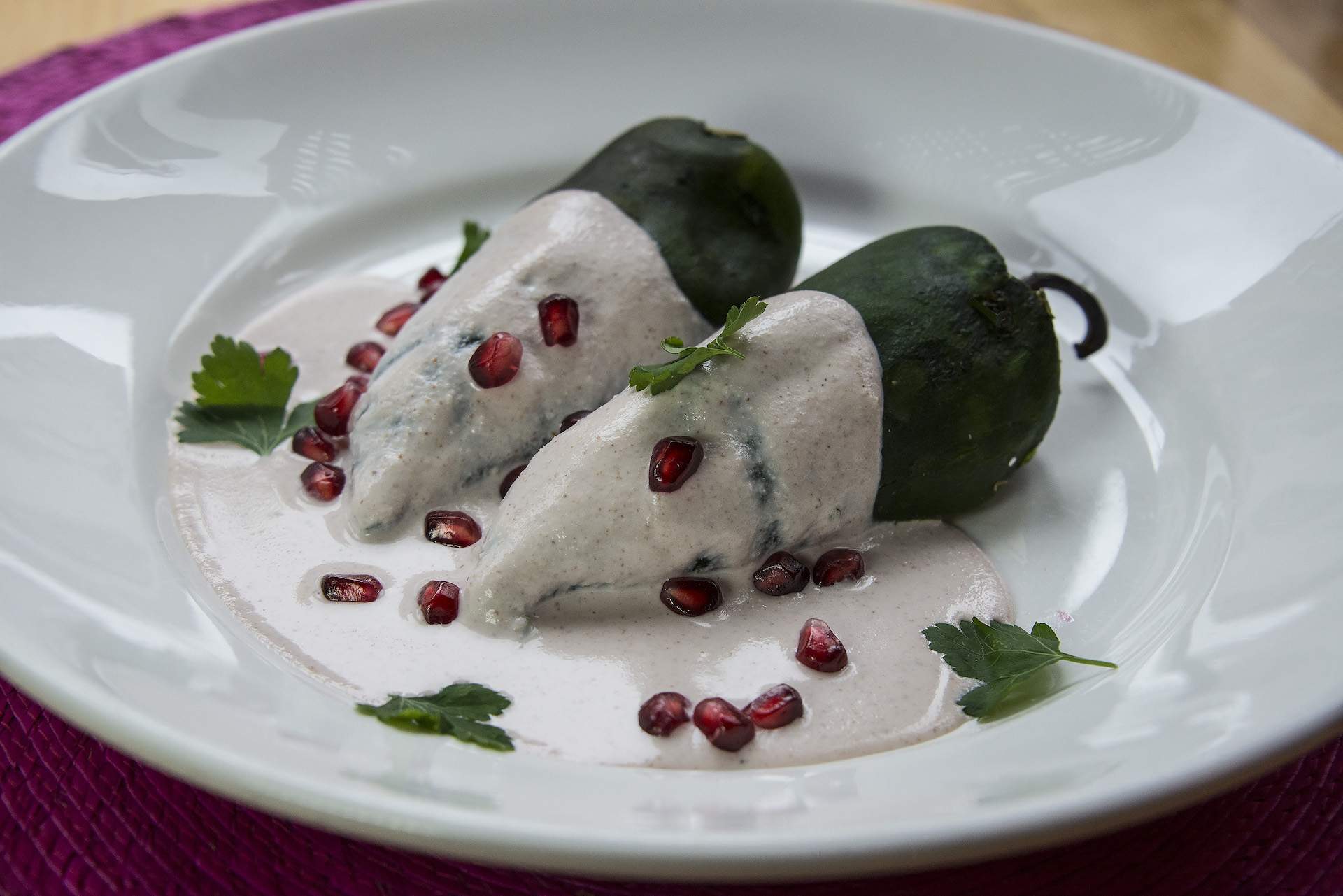 A chiles en nogada dish at NYC restaurant Fonda with two green peppers sitting in a white sauce and pomegranate seeds sprinkled on top.
