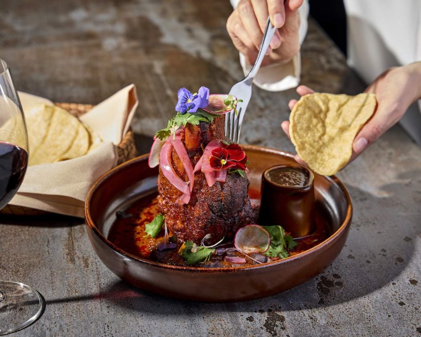 A hand holding a fork shredding some meat from a cochinita pibil dish at Chicago Mexican restaurant Tzuco.