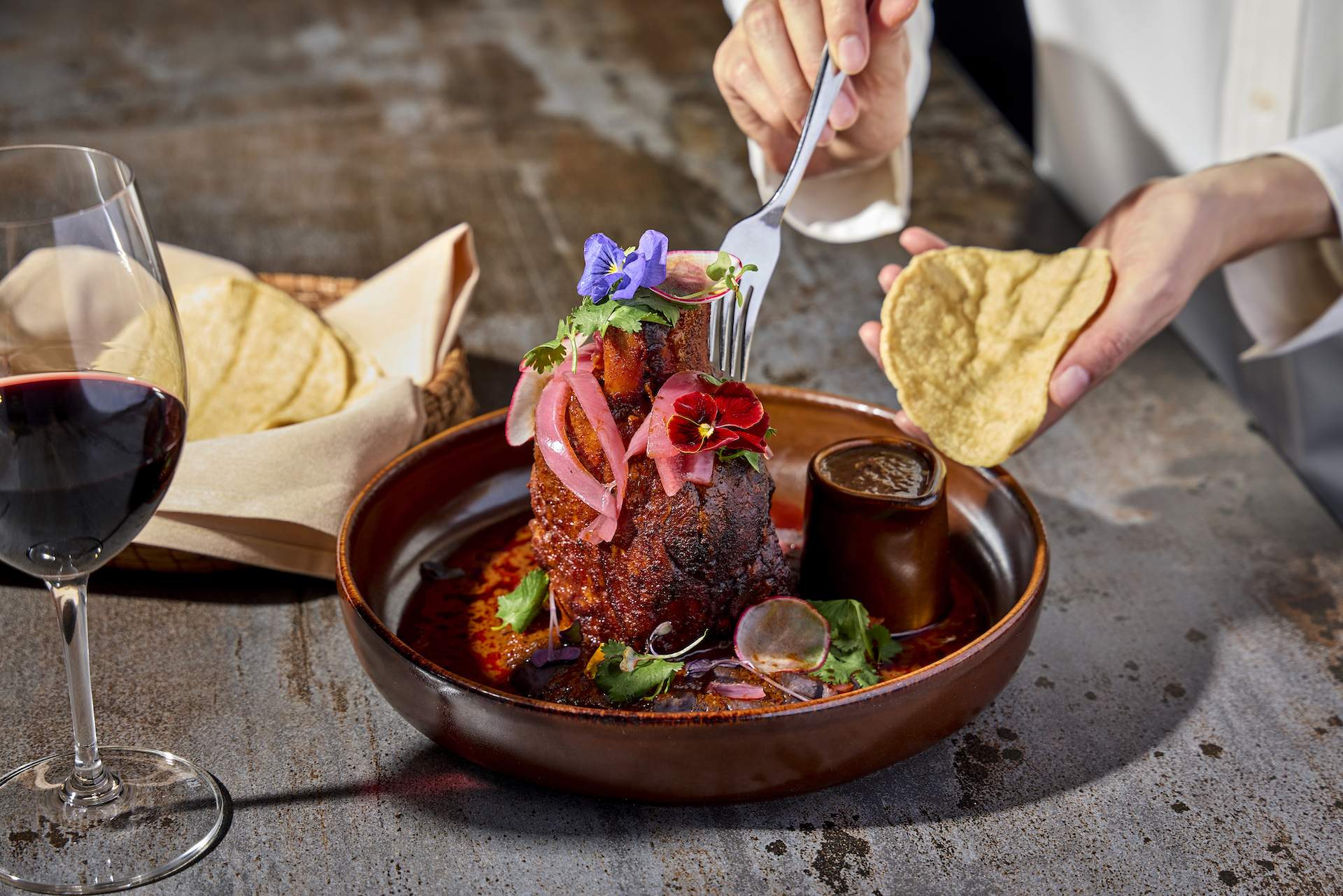 A hand holding a fork shredding some meat from a cochinita pibil dish at Chicago Mexican restaurant Tzuco.