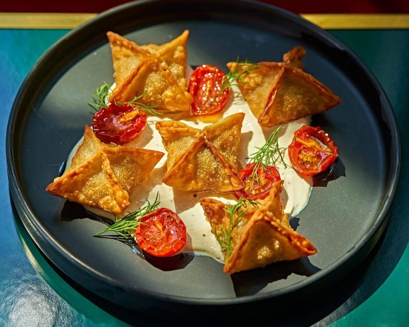 Fried dumplings called manti on a black plate with sliced tomatoes and a white sauce underneath at New York City restaurant Zou Zou’s.