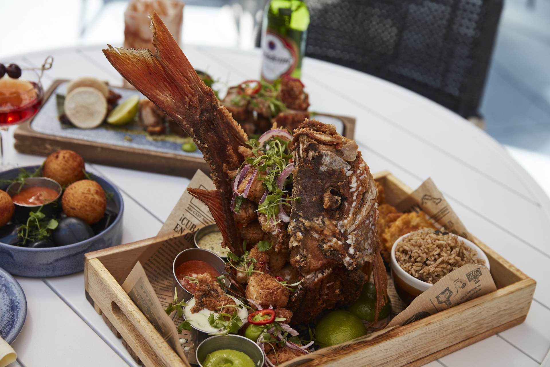 A whole fried fish placed on a wooden tray with condiments in small bowls around it at NYC Dominican restaurant Jalao.