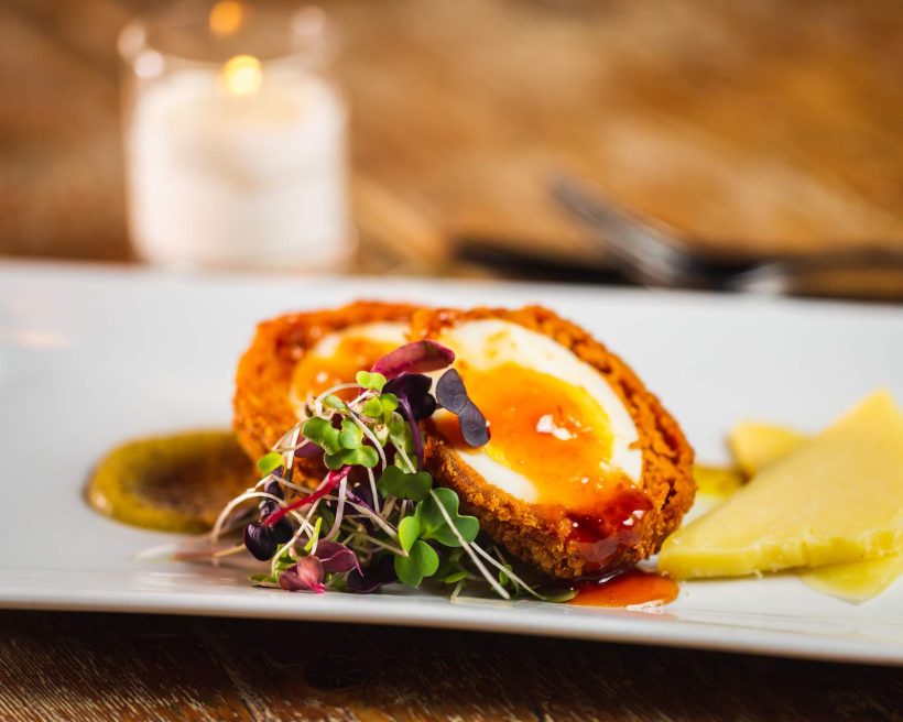 A close up of a Scotch egg dish, showing an egg sliced in half next to a piece of cheese and mustard sauce, at NYC restaurant Fraunces Tavern