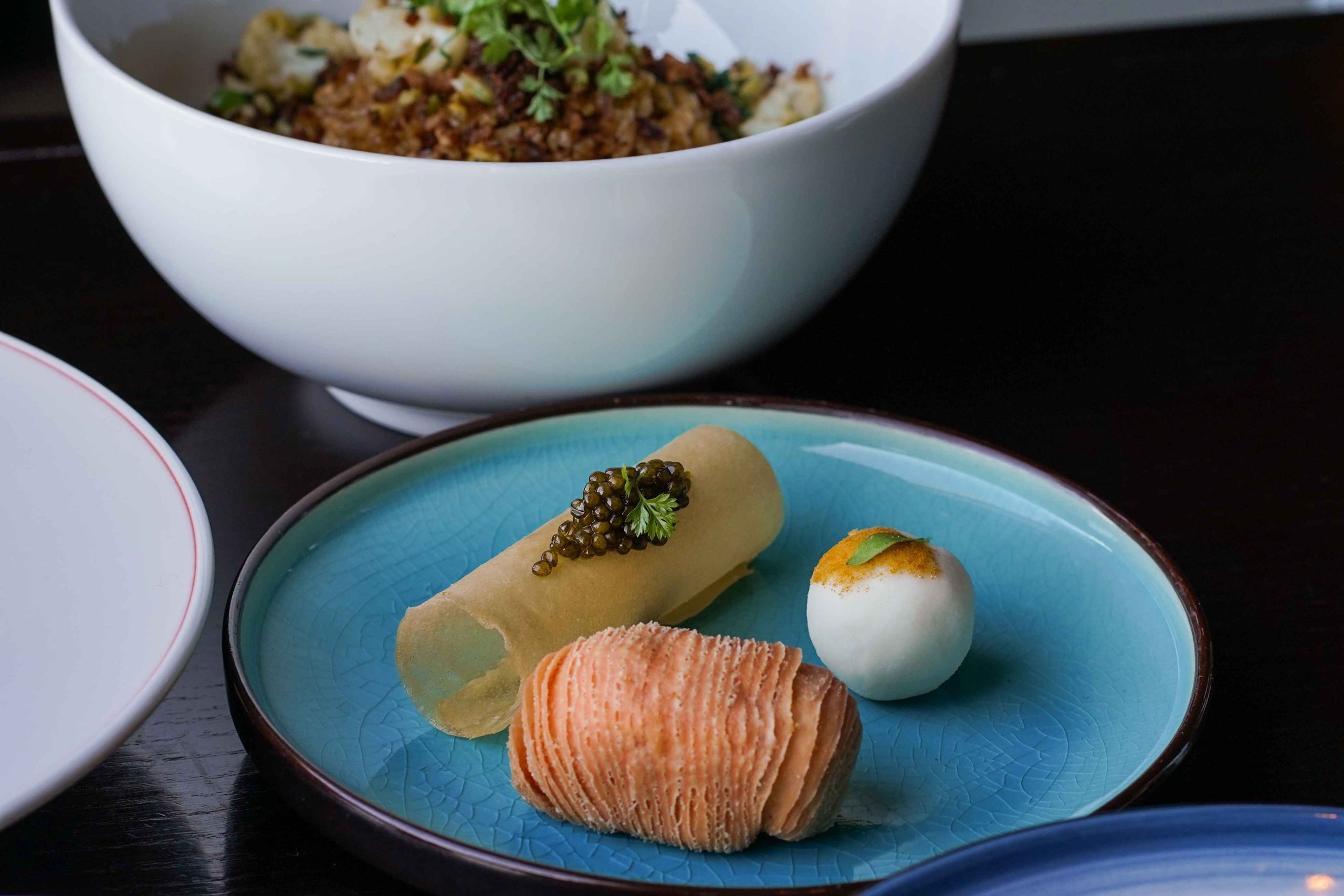 A scallop and kaluga caviar roll, lobster puff, and chilled fresh lily bulb on a blue plate at The Empress by Boon in San Francisco