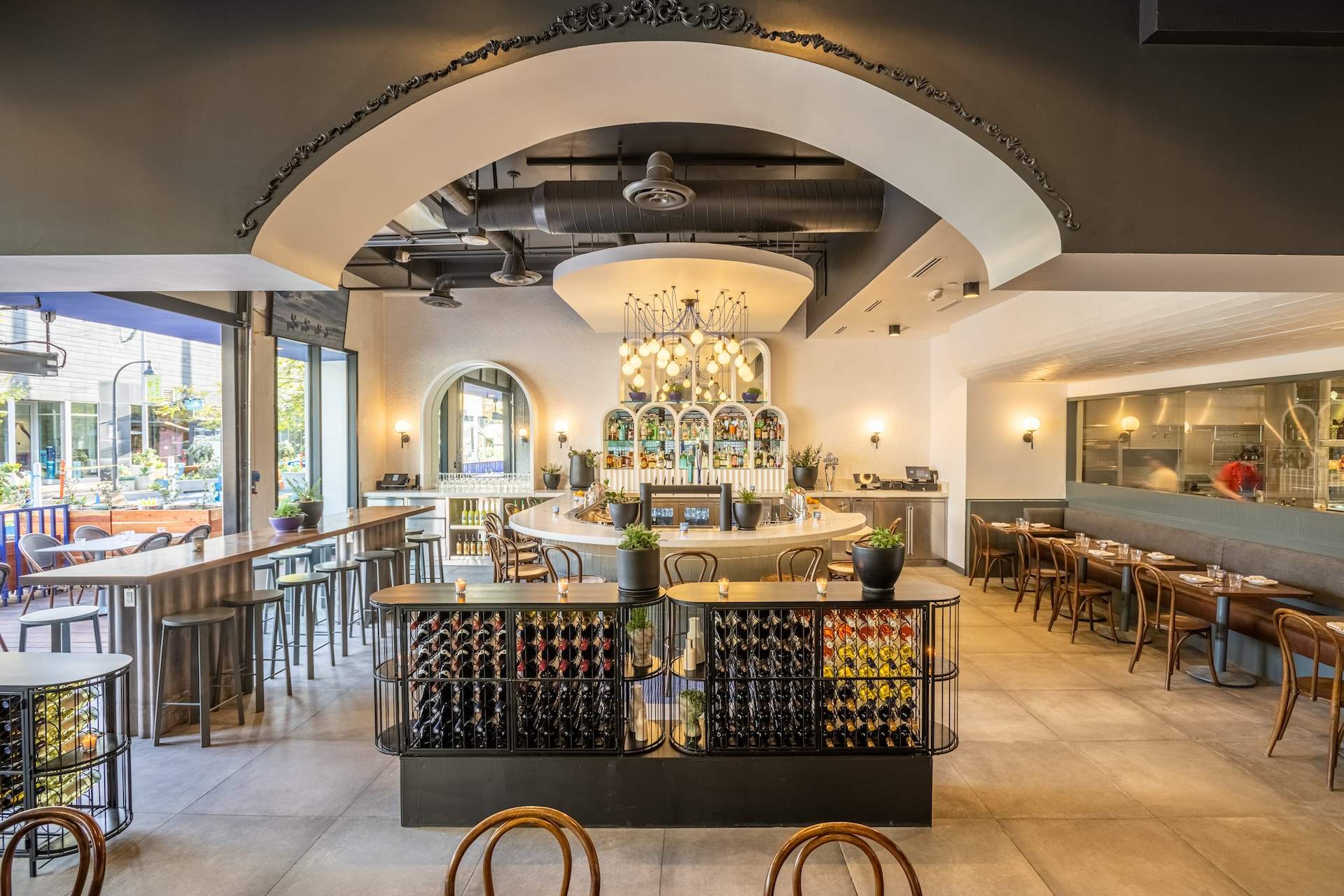 The interior of Los Angeles restaurant Superfine Playa with wine bottles stored in the foreground and a chandelier over a horseshoe bar in the background